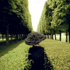 a woman wearing a black dress and hat standing in the middle of a green field