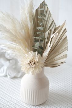 a white vase with some flowers and feathers in it on a tableclothed surface