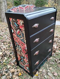 an old dresser has been painted with colorful designs and is sitting in the leaves on the ground