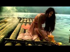 a woman sitting on top of a bamboo raft next to a lake holding a lit candle