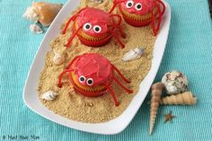 three red crabs in the sand with shells and seashells around them on a blue table cloth