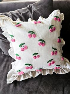 a white pillow with pink flowers on it sitting on a gray couch next to pillows