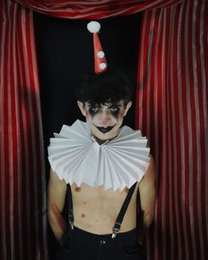 a man with clown makeup and paper fan around his neck, standing in front of red curtains