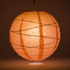 a large orange paper ball hanging from a light fixture with wires running through it, on a dark background