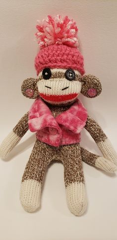 a sock monkey with a pink scarf and hat on it's head is posed in front of a white wall