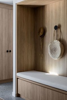 a wooden bench with a white cushion and hat hanging on it's back wall