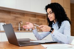 a woman sitting at a table in front of a laptop pointing to something on the screen