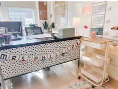 a desk with a sign that says mrs phillips on it and some shelves in the background