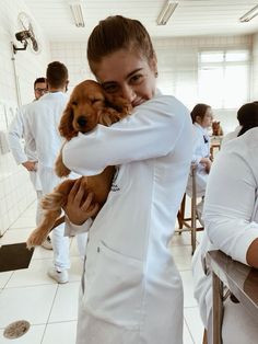 a woman in white lab coat holding a brown dog while standing next to another person