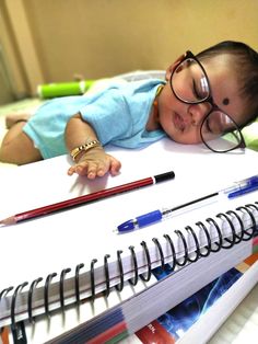 a small child laying on top of a bed next to a notebook and pencils