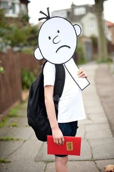 a young boy with a backpack and paper cut out of his face standing on the sidewalk