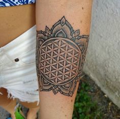 a woman's leg with a flower of life tattoo on her left arm and the symbol of the flower of life in the center