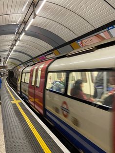 a train traveling through a subway station next to people on the platform with their luggage