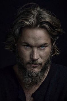 a man with long hair and blue eyes wearing a black shirt is looking at the camera