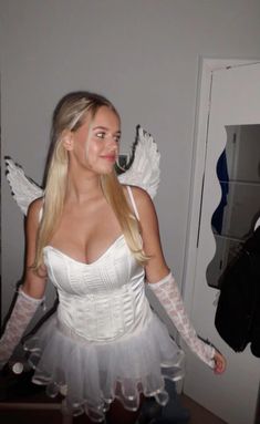 a woman in a white corset and angel wings is standing near a mirror