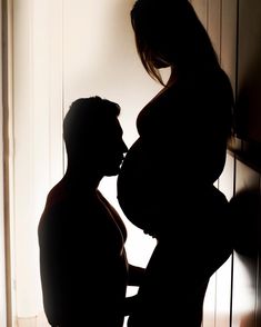 a pregnant woman standing in front of a door with her shadow on the wall behind her