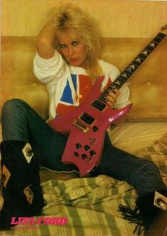 a woman sitting on top of a bed holding a pink guitar in her hand and looking at the camera