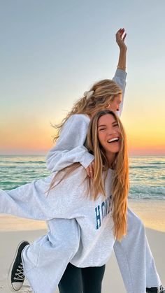 two girls are playing on the beach at sunset