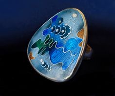 A gorgeous handcrafted enamel ring with primarily blue colors and other colorful accents. The ring has an engraved starburst pattern underneath the glass to give it a beautiful depth and texture.  Please feel free to ask me any additional questions you may have. Blue Oval Enamel Rings, Contemporary Blue Jewelry For Gifts, Artistic Blue Enamel Jewelry, Artistic Hand Painted Silver Rings, Unique Handmade Multicolor Enamel Ring, Modern Multicolor Handmade Rings, Unique Hand Painted Rings, Artsy Blue Enamel Jewelry, Unique Multicolor Enamel Ring