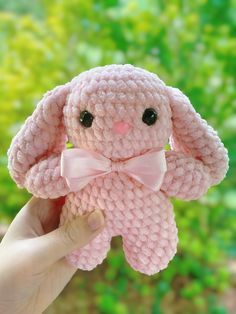 a hand holding a pink crocheted bunny with a bow on it's head