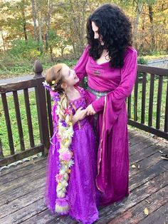 mother and daughter dressed up as princesses standing on deck in front of wooded area