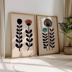 two framed art pieces on a shelf next to a potted plant in a room