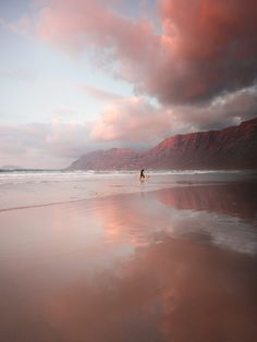 a person is walking on the beach with a surfboard under a pink and blue sky