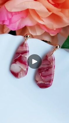 the pink and white earrings are on display next to a large rose flower in front of it