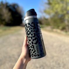 a person holding up a black and white leopard print water bottle in the middle of an empty road