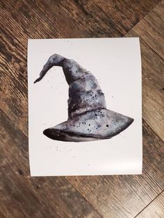 a watercolor drawing of a wizard's hat on a piece of paper that is sitting on a wooden floor