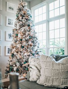 a living room with a white christmas tree and pictures on the wall above it, in front of a window