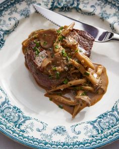 a steak with gravy and french fries on a blue and white china plate