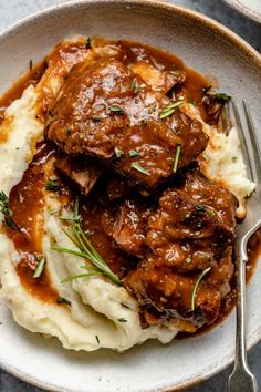 meat and mashed potatoes with gravy in a white bowl on a table