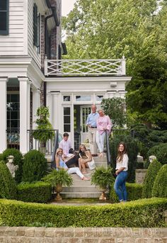 a group of people sitting on steps in front of a house with bushes and trees