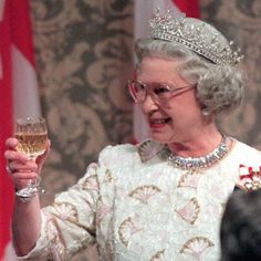 an older woman wearing a tiara and holding a glass of wine in front of flags