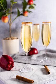 two glasses of champagne with cinnamons and apples in the background on a marble table