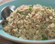 a blue bowl filled with rice and nuts on top of a wooden table next to a spoon