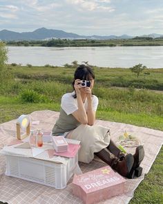 a woman sitting on top of a blanket holding a camera next to a box and boxes