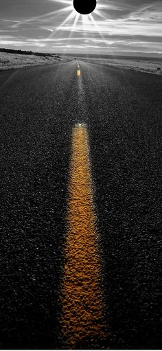 the sun is shining down on an empty road with a yellow line in the middle