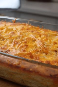 a cheesy casserole in a glass dish on top of a wooden table