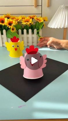 someone is making a paper chicken craft on a table with sunflowers in the background