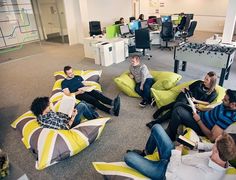 a group of people sitting on bean bag chairs in an office setting with computers and monitors