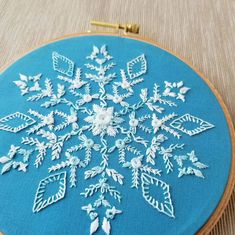 a snowflake is shown on a blue hoop hanging from a gold thread and it's stitched together