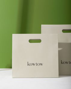 two white shopping bags with the words kowt on them sitting on a table in front of a green wall