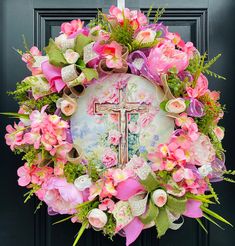 a wreath with pink flowers and a cross on it is hanging on the front door