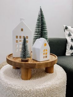 two small christmas trees sitting on top of a wooden table next to a white house