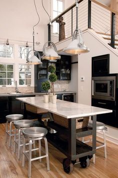 a kitchen island with stools and lights hanging from it's ceiling in front of an open floor plan