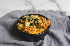 a black bowl filled with food sitting on top of a gray cloth next to a towel