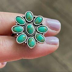 a close up of a person's hand holding a ring with turquoise stones on it