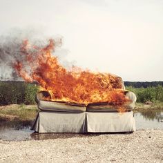 a couch covered in fire sitting on top of a gravel field